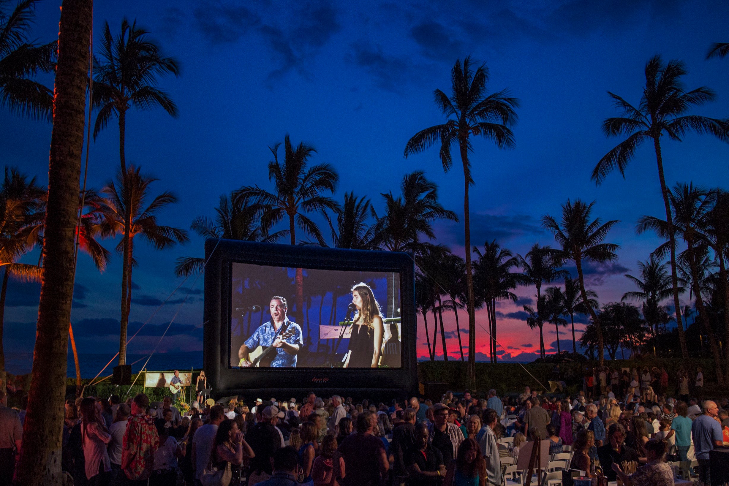 An outdoor movie audience gathered in front of an Open Air Cinema inflatable screen at dusk
