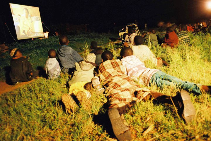 Audience gathered behind a large Open Air Cinema outdoor theater screen at a community event