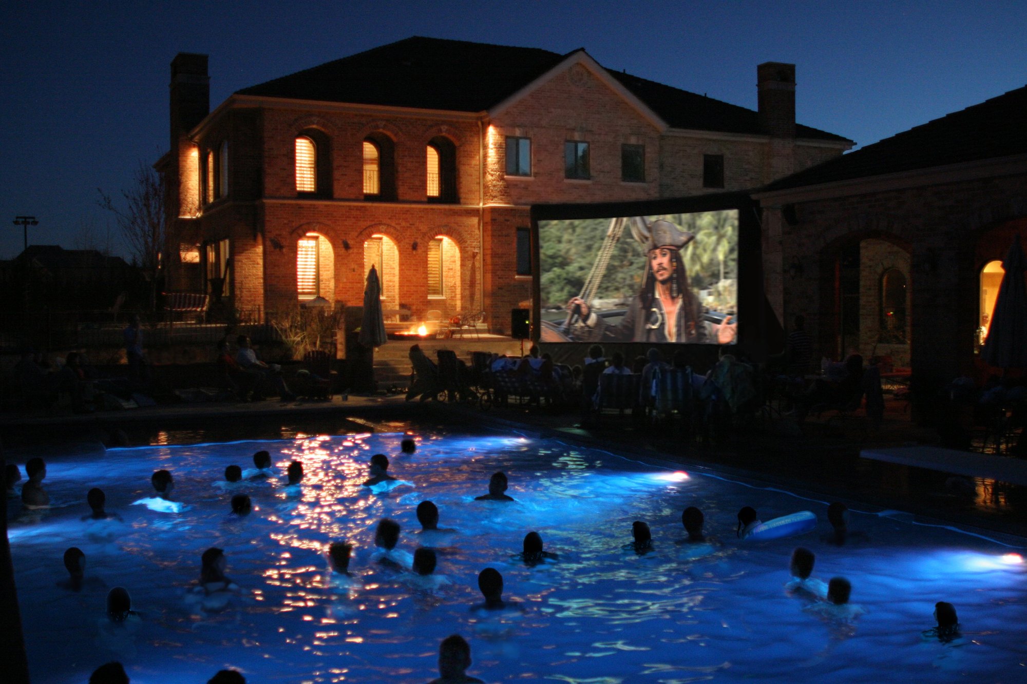 Guests watching a movie from a pool at night in front of an Open Air Cinema screen